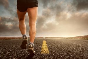 Runner's legs on a road during a sunset, symbolizing endurance and outdoor fitness training.