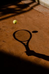 A tennis racket shadow and tennis ball on a clay court surface, capturing the essence of the sport.