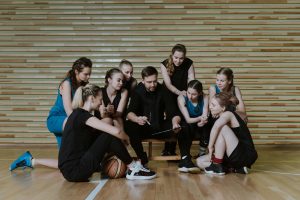 A coach strategizes with a women's basketball team in a gymnasium.